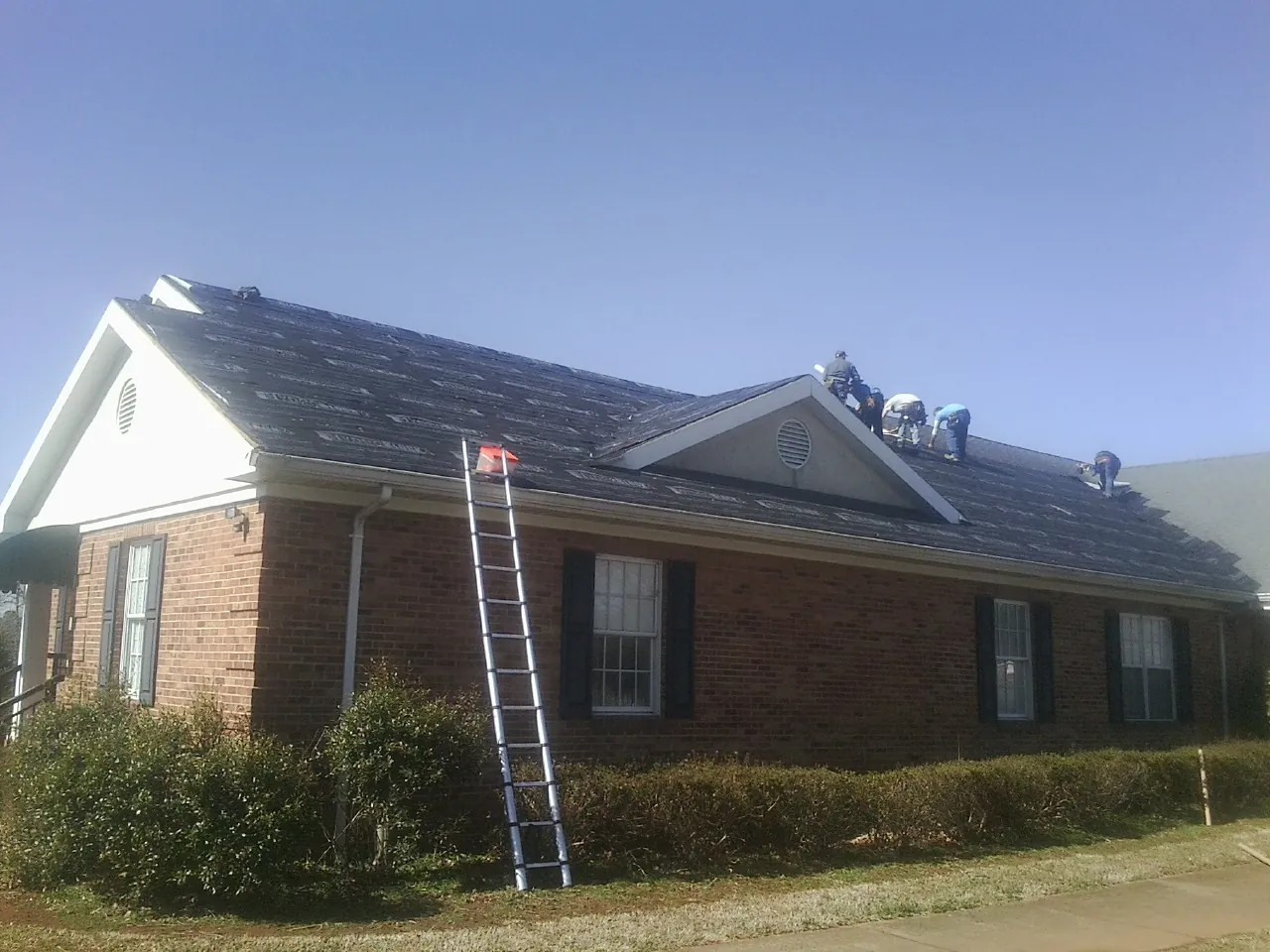 Crew tearing shingles off a brick ranch roof with a ladder set — Metal Roof Repair work by our crew in Darien