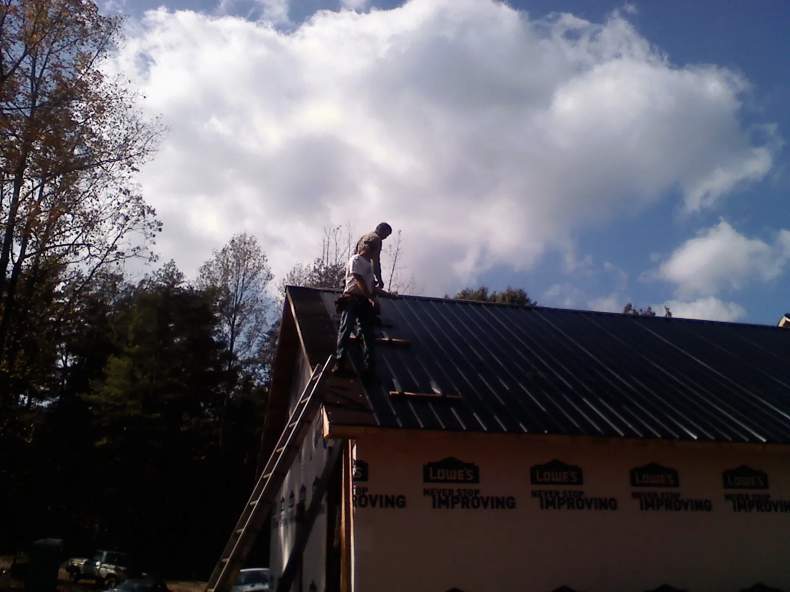 Roofer fastening dark metal panels high against a cloudy sky, from a Roof Inspection job in Darien